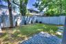 Enclosed backyard featuring a paver patio, stone-finish walkway, white privacy fencing, and mature trees