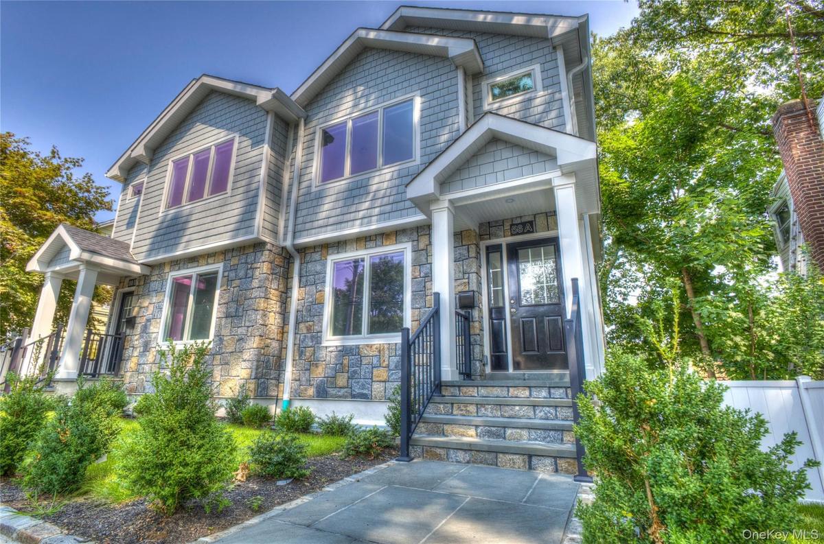 Multi-story exterior featuring stone veneer siding, shingle-style upper cladding, a covered entry with white columns, and a stone-paved walkway