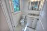 White cabinetry vanity with stone-composite countertop, undermount sink, metallic faucet, rectangular wall-mounted mirror, and stone-patterned tile fl