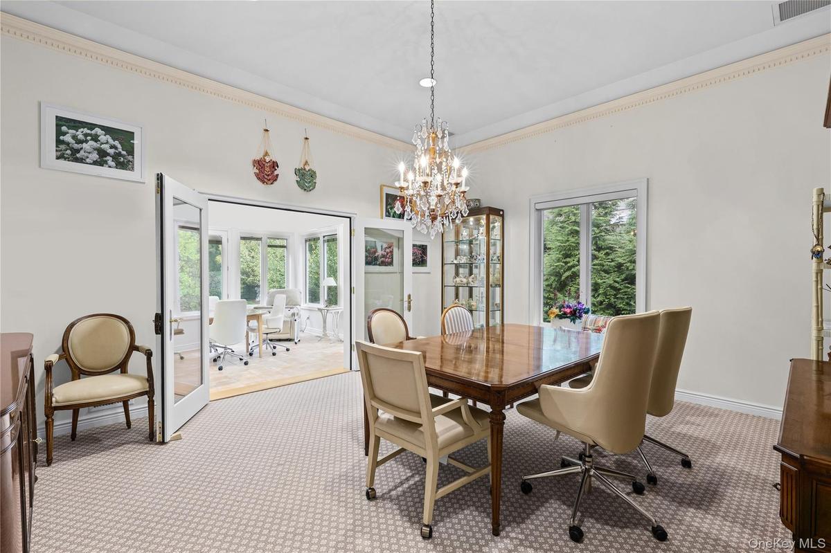 Dining area featuring crown molding, a central crystal chandelier, double glass-paneled doors, and large windows
