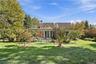 Rear exterior featuring a multi-gabled roofline, ground-level stone patio, and glass-paned double doors set amidst expansive landscaped grounds with m