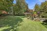 Expansive backyard featuring a manicured lawn, mature trees, a natural stone wall boundary, and varied perennial landscaping