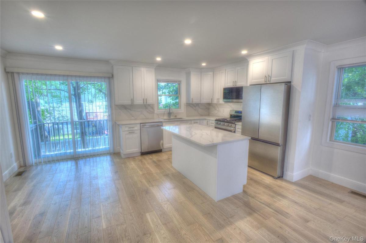 Kitchen featuring shaker-style cabinetry, a central island with a stone-finish countertop, stainless steel appliances, and wood-finish flooring
