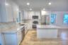 Kitchen featuring white shaker-style cabinetry, stone-finish countertops with integrated backsplash, a central island, stainless steel appliances, and