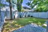 Private backyard featuring a paved stone patio, mature trees, manicured lawn, and full-perimeter vinyl fencing