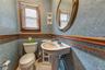 Powder room/half bath with Pedestal sink with chrome faucet, oval wall-mounted mirror, wood-trimmed window.