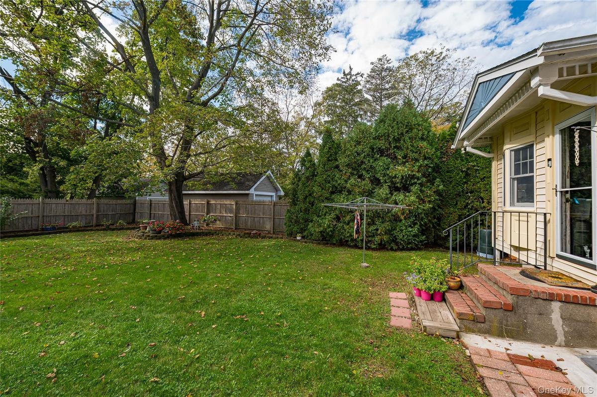 Private backyard featuring a level lawn, mature trees, wood privacy fencing, and a brick-stepped entrance