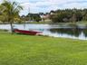 Waterfront lot featuring a manicured lawn, natural pond, boulder accent, and mature palm trees
