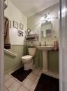 Ceramic tile flooring, pedestal sink with metal faucet, beadboard wainscoting, arched wall-mounted mirror, and three-bulb vanity lighting