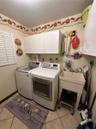 Laundry area featuring white cabinetry, a freestanding utility sink with faucet, ceramic tile flooring, and plantation shutter window coverings