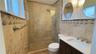 Bathroom featuring natural stone wall tile with decorative accent border, a glass-enclosed shower with a rainfall showerhead, and a vanity with a whit