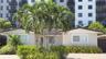 Single-story exterior featuring a light-colored stucco facade, tiled roof, paver driveway, and mature tropical landscaping