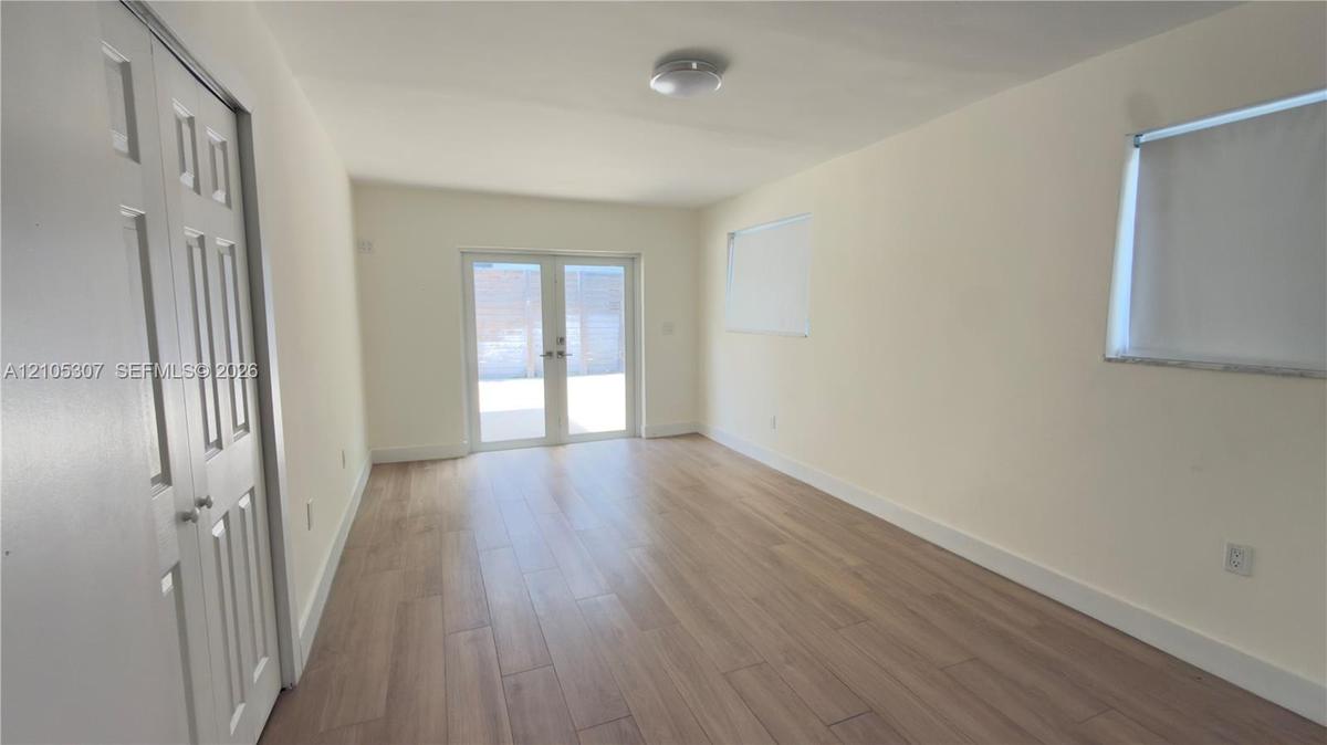 Interior space featuring light-toned wood-finish flooring, dual-panel closet doors, white walls, and French doors leading to a paved patio area