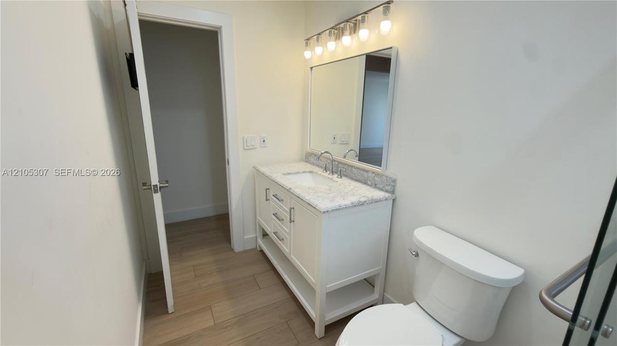 Bathroom vanity featuring stone-finish countertop, integrated sink, and white cabinetry, accompanied by a rectangular mirror, five-light fixture, and 