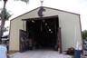 Metal-sided outbuilding featuring a high-clearance entrance, swinging door mechanisms, and a decorative roof-mounted weather vane