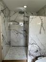 Walk-in shower featuring large-format stone-finish wall tile, hexagonal floor tiling, a rainfall showerhead, and a linear floor drain