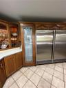 Custom wood cabinetry, floor-to-ceiling pantry with etched glass door, integrated side-by-side stainless steel refrigeration, and ceramic tile floorin