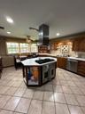 Kitchen featuring a hexagonal island with an integrated cooktop and oven, stainless steel range hood, stone-finish tile flooring, recessed lighting, a
