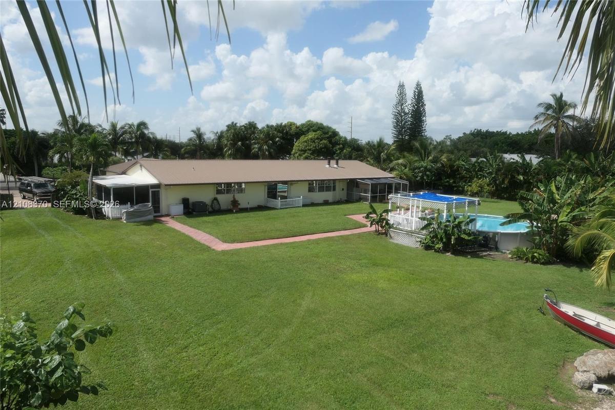 Expansive backyard featuring a large grass lawn, screened-in patio, and an above-ground swimming pool with a hardscape surround