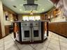 Kitchen featuring a central island with a built-in stainless steel double oven, glass-paned range hood, tile flooring, and custom cabinetry with integ