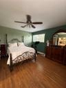 Room featuring wood-finish flooring, a multi-blade ceiling fan with integrated light fixture, and a single-pane window with a grid pattern