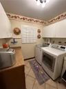 Laundry room featuring white shaker-style wall cabinetry, a laminate countertop, tile flooring, and a window with plantation-style shutters