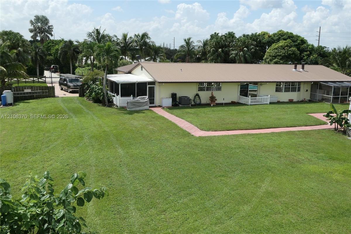 Expansive lawn with mature trees, metal roofing, and multiple screened-in enclosures