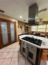 Kitchen featuring a center island with a built-in stainless steel gas cooktop, overhead stainless steel vent hood, pantry with decorative glass-panel 