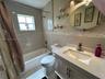 Bathroom featuring a vanity with a solid-surface countertop, an integrated sink, an oval wall-mounted mirror, neutral tile wall surround with decorati