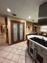 Kitchen featuring double doors with frosted glass panels, stainless steel gas range with overhead vent hood, ceramic tile flooring, and built-in cabin