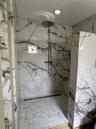 Walk-in shower featuring large-format veined tile surround, recessed wall niche, rain-style shower head, linear floor drain, and hexagonal tile floori