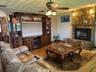 Living area featuring a floor-to-ceiling natural stone fireplace with a raised hearth, wood-finish flooring, built-in wooden media cabinetry, and a ce