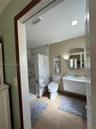 Walk-in shower with floor-to-ceiling veined tile surround, recessed wall shelving, wall-mounted vanity, and wood-finish flooring