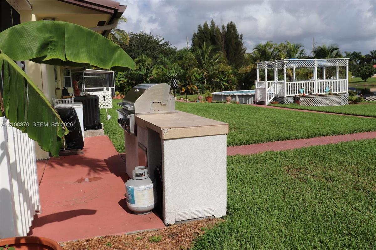 Outdoor kitchen featuring a built-in grill and concrete countertop, expansive lawn, swimming pool, and white lattice gazebo