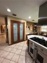 Double pantry with frosted glass paneled doors, stainless steel gas range with overhead ventilation hood, recessed lighting, and tile flooring