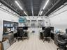 Office space featuring an exposed truss ceiling, industrial-style lighting, neutral wood-finish flooring, and integrated windows providing visibility 
