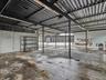 Expansive open-concept industrial space featuring a corrugated metal roof, steel structural support columns, and concrete flooring