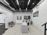 Open-concept interior featuring a high, black exposed-joist ceiling, white stacked-stone accent wall, wood-finish flooring, linear LED lighting, and a