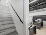 Staircase with wood-finish treads and metal trim, sleek black handrail, and open-plan area featuring exposed industrial ceiling trusses