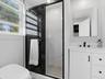 Bathroom featuring a shower with a black-framed glass enclosure, light-toned stone-finish tile surround, white vanity with matte black hardware, and a