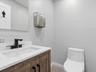 Wood-finish cabinetry featuring black hardware, white countertop with integrated rectangular sink, matte black widespread faucet, wall-mounted stainle
