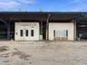 Industrial facility featuring dual-bay modular enclosures, metal roof canopy, exhaust ventilation systems, and expansive concrete exterior surface