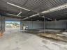 Open-concept warehouse space featuring high-clearance metal corrugated roofing, concrete flooring, support columns, and a large roll-up entry door
