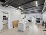 Open-concept space featuring an exposed black corrugated metal ceiling with industrial ductwork, linear LED lighting, wood-finish flooring, and white 