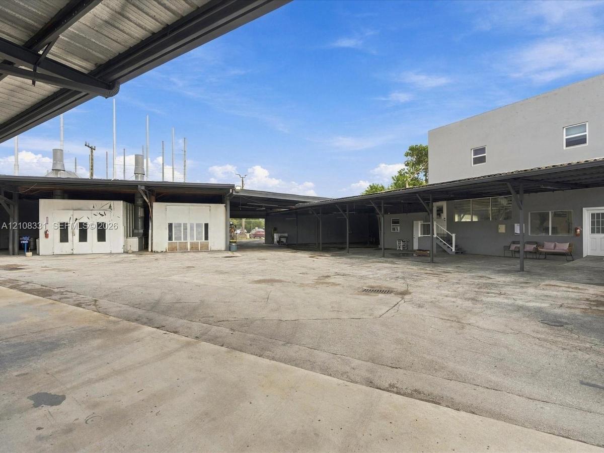 Expansive concrete exterior courtyard featuring extensive metal-framed covered parking, multi-level building structures, and industrial-style exterior