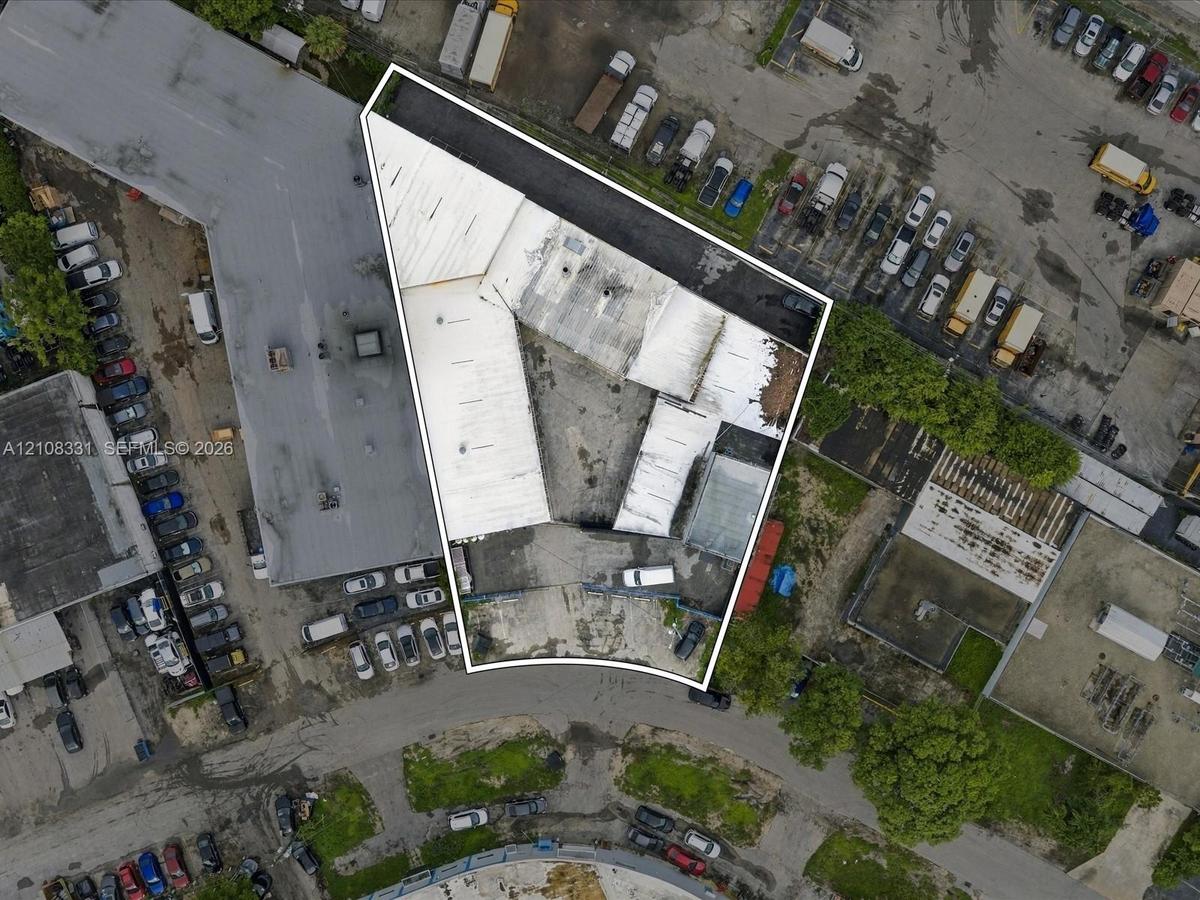 Aerial view of the parcel featuring a corner-lot orientation, paved exterior surface, and multiple attached industrial-style structures with flat roof