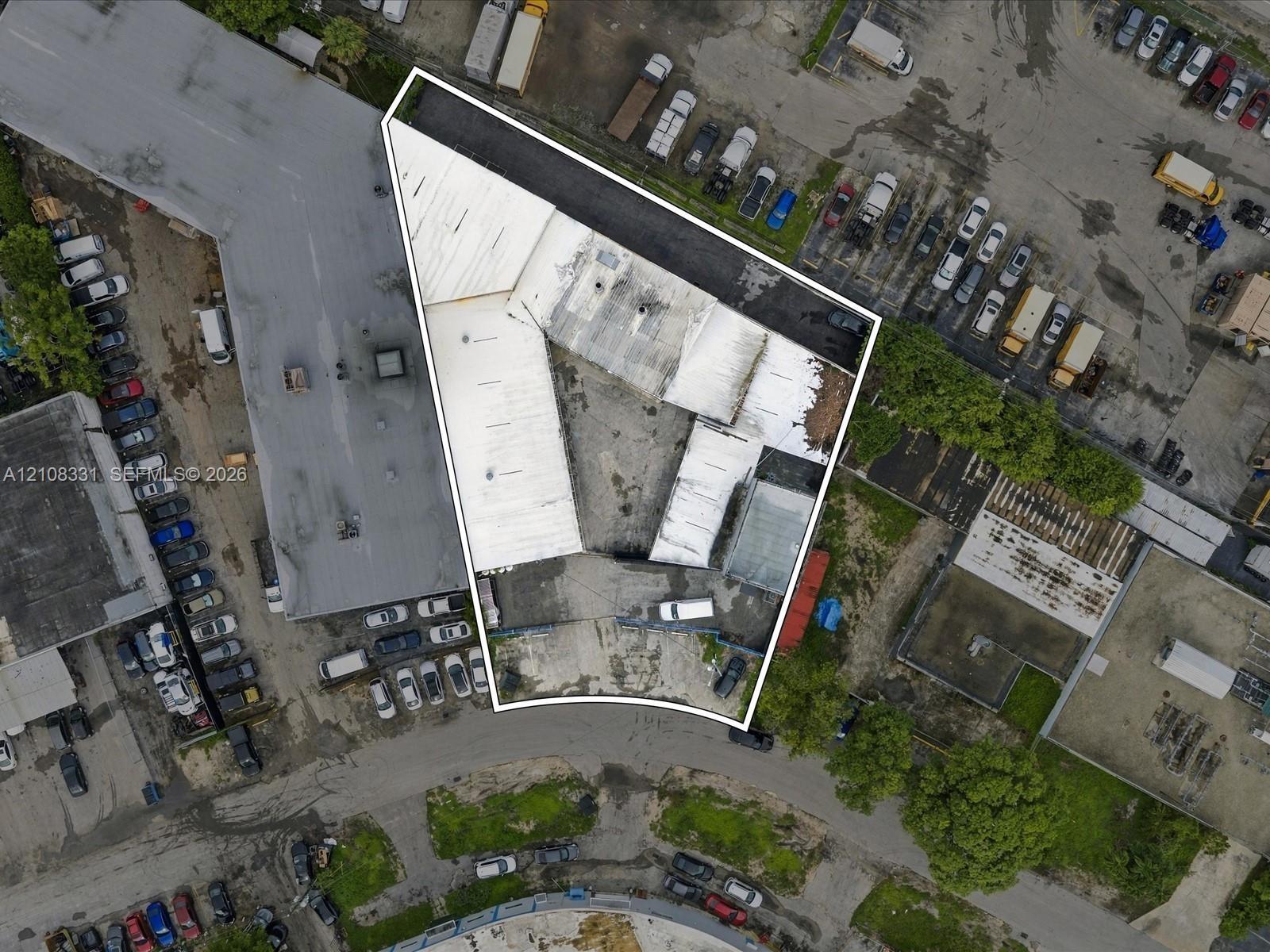 Aerial view of the parcel featuring a corner-lot orientation, paved exterior surface, and multiple attached industrial-style structures with flat roof
