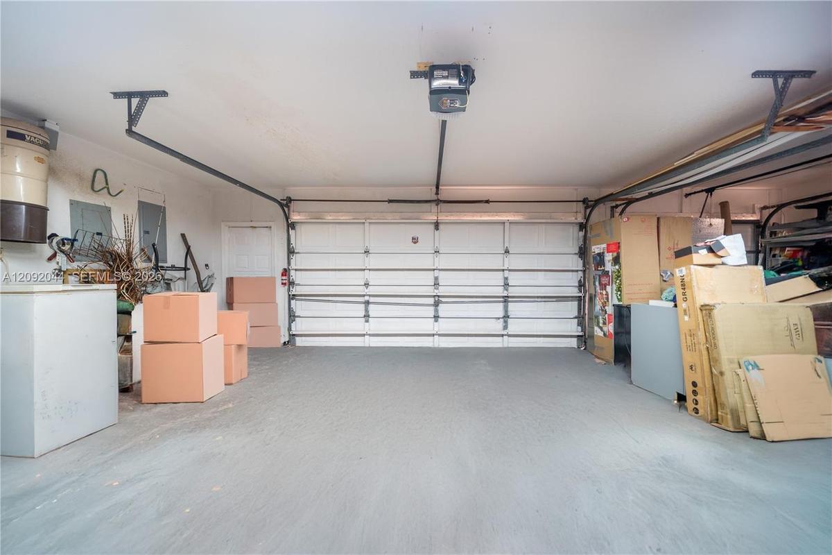 Attached two-car garage featuring a sectional overhead door, automated door opener, finished concrete flooring, and an integrated electrical panel