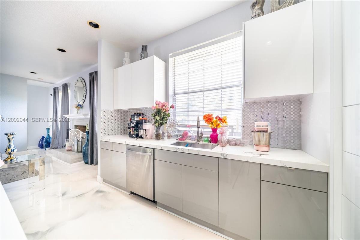 Kitchen featuring high-gloss cabinetry, stone-finish countertops, stainless steel appliances, patterned mosaic tile backsplash, and recessed lighting