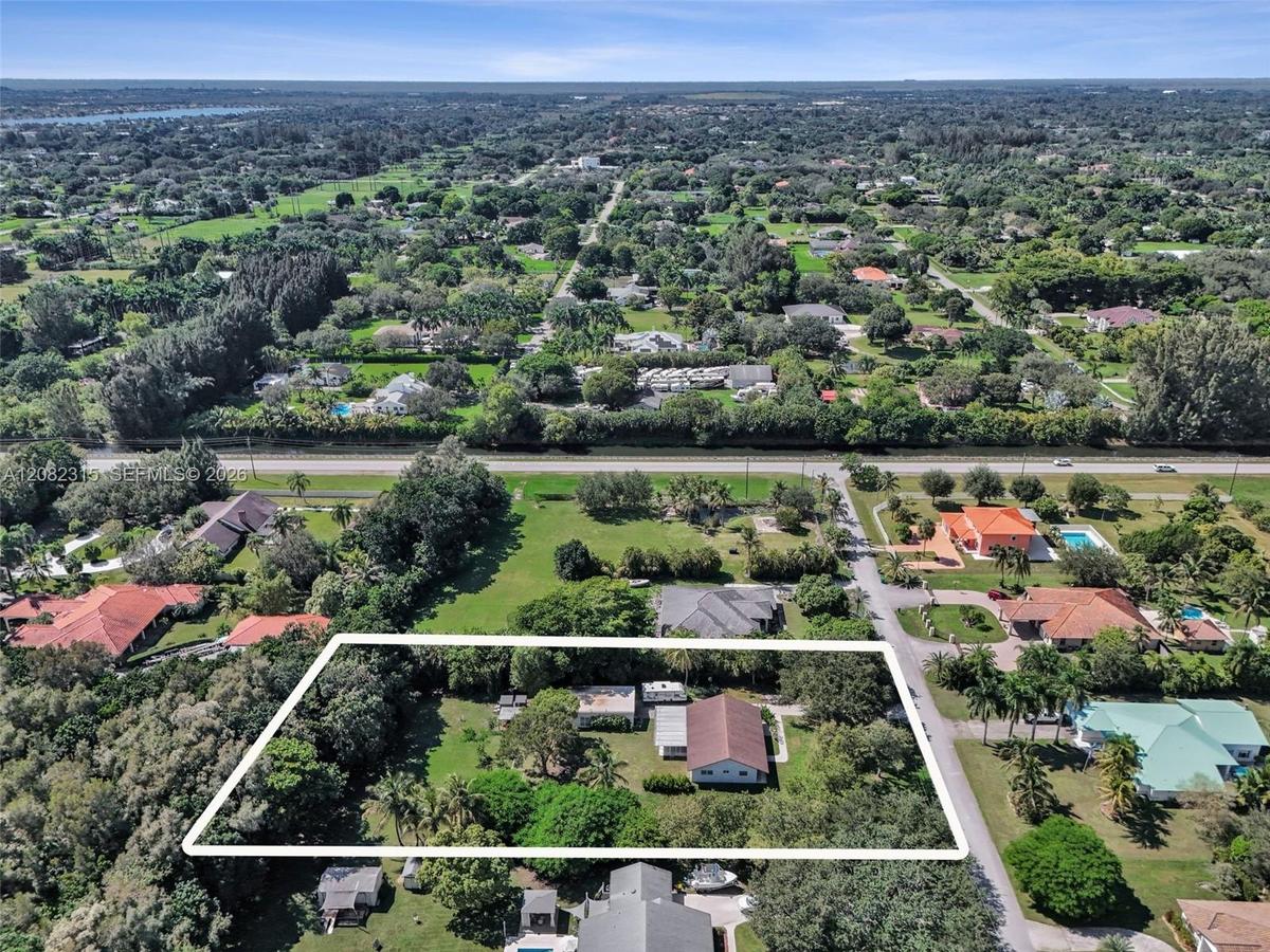Aerial perspective of a multi-structure property featuring mature trees, expansive green space, and a paved driveway